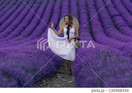 A woman in a white dress stands in a field of purple flowers 130986930