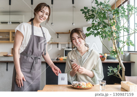 カフェでQRコードを提示する店員とスマホを操作する女性客 カフェでQRコードを提示する店員とスマホを操作する女性客 130987159