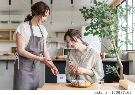 カフェでQRコードを提示する店員とスマホを操作する女性客 130987162