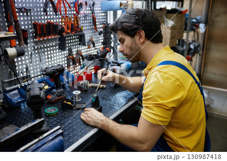 Skilled man worker is working on soldering iron in a workshop 130987418