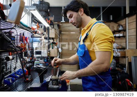 A skilled man is working on broken electrical equipment that is securely clamped in a vise 130987419