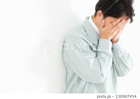 顔を覆って悩む作業着姿のミドル男性ビジネスマン 130987454
