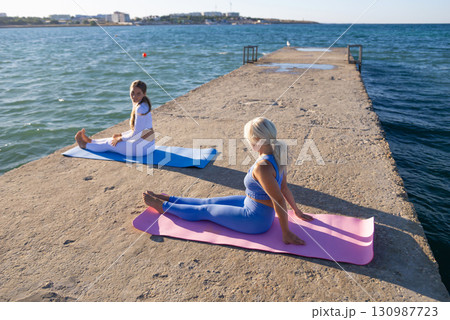 Yoga Women Pier - Two women practicing yoga on a pier overlooking the sea on a sunny day. 130987723