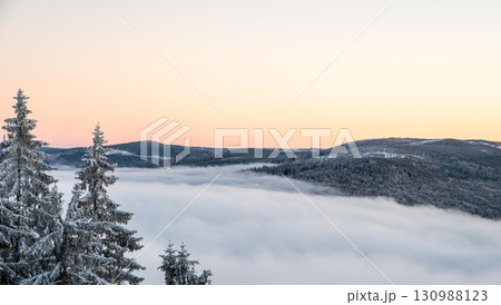 Winter inversion sunset with snow covered hills and forests rising above a sea of clouds, captured from above, with warm evening light painting the sky in glowing tones. Winter inversion sunset with snow covered hills and forests rising above a sea of clouds, captured from above, with warm evening light painting the sky in glowing tones. 130988123