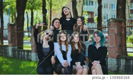 Group of seven stylish young women gather on a bench outside their high school, basking in the sunshine and each other's company 130988168