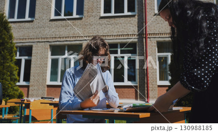 Two high school students collaborating on a project outdoors, embracing the sunshine and fresh air at their school 130988185