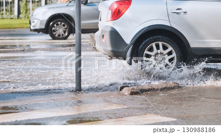 Suv driving through large puddle on pedestrian crossing, creating big splash of water after rain 130988186