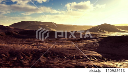 Golden sunlight casts vibrant hues over rugged mountain terrain at twilight. The serene landscape showcases varied textures of earth and rock beneath a bright sky filled with clouds. Golden sunlight casts vibrant hues over rugged mountain terrain at twilight. The serene landscape showcases varied textures of earth and rock beneath a bright sky filled with clouds. 130988618