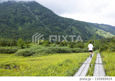 木道をハイキングする男性 130989424