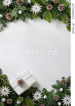 Christmas frame with evergreen branches and carving wooden eco natural decorations, snowflakes, pine cones on white background. Copy space. Xmas vertical greeting card. Winter Holiday. View from above Christmas frame with evergreen branches and carving wooden eco natural decorations, snowflakes, pine cones on white background. Copy space. Xmas vertical greeting card. Winter Holiday. View from above 130990129