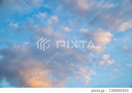 White fluffy clouds float gently in a clear blue sky on a bright sunny day. The scene feels open clean and refreshing. 130990563