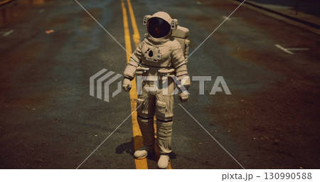 An astronaut stands confidently on a deserted city street, the asphalt glistening after rain. This unexpected presence evokes a sense of wonder in an ordinary urban setting. 130990588