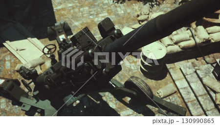 A heavy artillery piece stands ready on the battlefield, surrounded by sandbags and debris. Sunlight casts shadows on the ground, depicting a critical moment in a military operation. A heavy artillery piece stands ready on the battlefield, surrounded by sandbags and debris. Sunlight casts shadows on the ground, depicting a critical moment in a military operation. 130990865