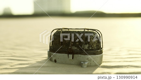 A weathered metal object rests on a shore of fine sand, illuminated by the golden light of the setting sun. The surface shows signs of wear, blending with the tranquil surroundings. A weathered metal object rests on a shore of fine sand, illuminated by the golden light of the setting sun. The surface shows signs of wear, blending with the tranquil surroundings. 130990914