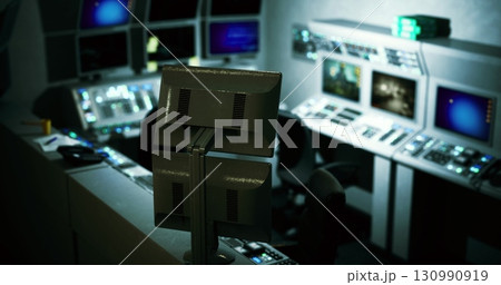 A dimly lit control room features multiple monitors displaying various data and graphics. The sophisticated setup suggests a hub for managing complex operations or systems. 130990919