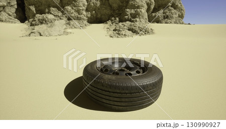 A lone tire lies on the sandy ground, surrounded by textured rocks under a blue sky, indicating a remote location possibly affected by abandonment or a vehicle breakdown. A lone tire lies on the sandy ground, surrounded by textured rocks under a blue sky, indicating a remote location possibly affected by abandonment or a vehicle breakdown. 130990927