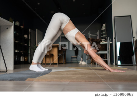 Woman practicing yoga pose downward dog at home, stretching body, focusing on flexibility, balance, strength, posture, breathing and healthy lifestyle for energy, calm and wellness. 130990968