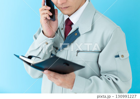 手帳を見ながらスマホで通話する作業着姿のミドル男性ビジネスマン 130991227