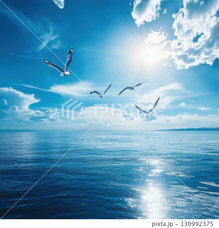 Seagulls flying over calm ocean waters under a bright blue sky with wispy clouds 130992375