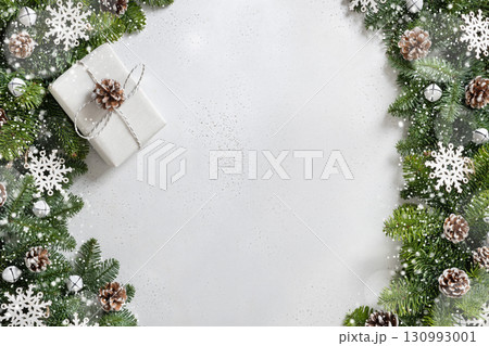 Christmas frame with white gift, evergreen branches and carving wooden snowflakes, pine cones on white background. Copy space. Xmas greeting card. Winter Holiday. View from above. Christmas frame with white gift, evergreen branches and carving wooden snowflakes, pine cones on white background. Copy space. Xmas greeting card. Winter Holiday. View from above. 130993001