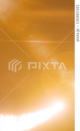 Bright golden lens flare and sunburst effect creating soft glowing orbs on an amber background 130993381