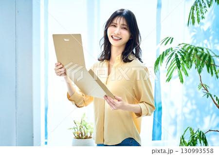 部屋で通販の荷物を確認をする女性のライフスタイルイメージ 130993558