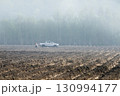 Farmers prepare to plant crops on their plowed agricultural land in a light foggy morning. 130994177