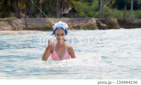 Girl in snorkel mask gives a thumbs up while swimming in bright tropical ocean waters Girl in snorkel mask gives a thumbs up while swimming in bright tropical ocean waters 130994236