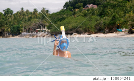 Young girl in pink swimsuit with snorkel mask proudly shows off starfish while exploring a tropical shoreline  130994241