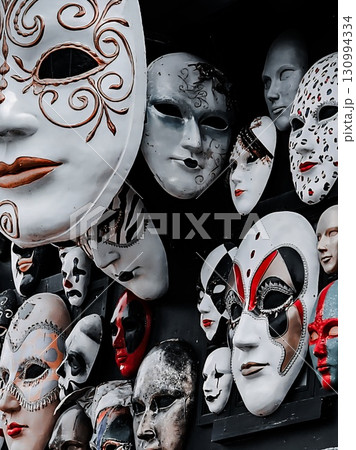 A unique and intriguing collection of many different masks hanging on a dark wall. 130994334
