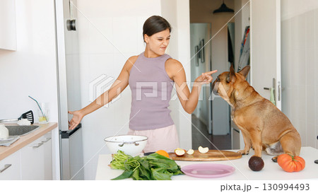 A woman is happily cooking in the kitchen, accompanied by her loyal dog companion nearby 130994493
