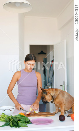 A woman happily cooking alongside her dog in a modern and vibrant kitchen setting 130994517