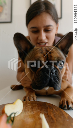 A girl joyfully interacts with her French Bulldog in a cozy kitchen, sharing playful moments 130994531