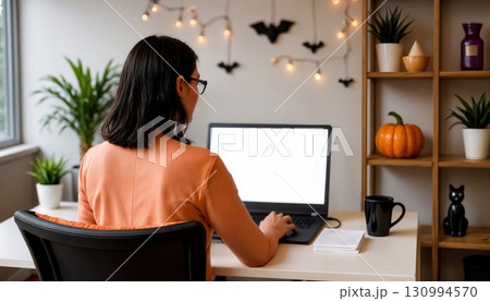 Young businesswoman working on laptop in room decorated for Halloween, monitor mockup, rear view 130994570