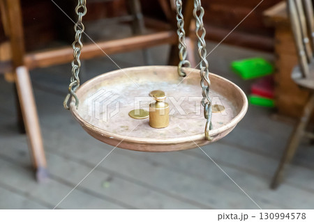 weight and gold coin on brass scales on a chain, scales close-up weight and gold coin on brass scales on a chain, scales close-up 130994578