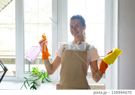 Woman Portrait in rubber gloves and apron manually washes window balcony of house with rag cleaner and mop inside interior. Restoring order and cleanliness in spring, cleaning servise Woman Portrait in rubber gloves and apron manually washes window balcony of house with rag cleaner and mop inside interior. Restoring order and cleanliness in spring, cleaning servise 130994870