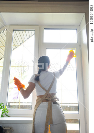 Woman in rubber gloves and apron manually washes window balcony of house with rag cleaner and mop inside interior. Restoring order and cleanliness in spring, cleaning servise Woman in rubber gloves and apron manually washes window balcony of house with rag cleaner and mop inside interior. Restoring order and cleanliness in spring, cleaning servise 130994898