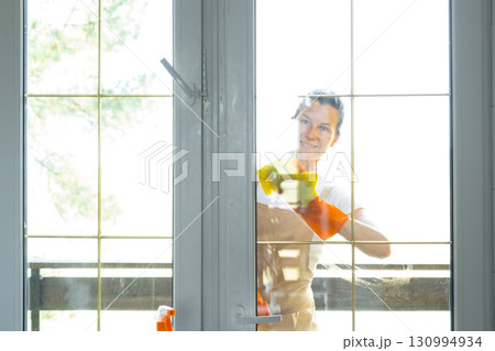 Woman in rubber gloves and apron manually washes window balcony of house with rag cleaner and mop outside behind glass. Restoring order and cleanliness in spring, cleaning servise Woman in rubber gloves and apron manually washes window balcony of house with rag cleaner and mop outside behind glass. Restoring order and cleanliness in spring, cleaning servise 130994934