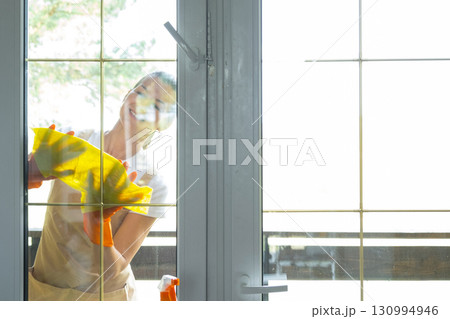 Woman in rubber gloves and apron manually washes window balcony of house with rag cleaner and mop outside behind glass. Restoring order and cleanliness in spring, cleaning servise Woman in rubber gloves and apron manually washes window balcony of house with rag cleaner and mop outside behind glass. Restoring order and cleanliness in spring, cleaning servise 130994946