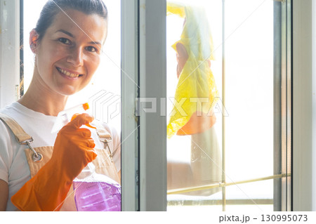 Woman Portrait in rubber gloves and apron manually washes window balcony of house with rag cleaner and mop inside interior. Restoring order and cleanliness in spring, cleaning servise Woman Portrait in rubber gloves and apron manually washes window balcony of house with rag cleaner and mop inside interior. Restoring order and cleanliness in spring, cleaning servise 130995073