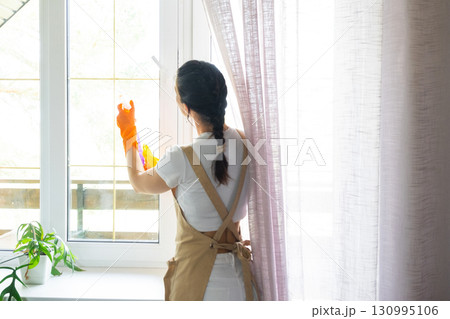 Woman in rubber gloves and apron manually washes window balcony of house with rag cleaner and mop inside interior. Restoring order and cleanliness in spring, cleaning servise Woman in rubber gloves and apron manually washes window balcony of house with rag cleaner and mop inside interior. Restoring order and cleanliness in spring, cleaning servise 130995106