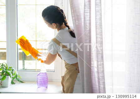 Woman in rubber gloves and apron manually washes window balcony of house with rag cleaner and mop inside interior. Restoring order and cleanliness in spring, cleaning servise Woman in rubber gloves and apron manually washes window balcony of house with rag cleaner and mop inside interior. Restoring order and cleanliness in spring, cleaning servise 130995114