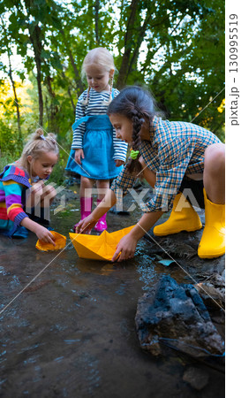 Kids with colorful rainboots launching paper boats in water play 130995519