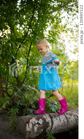 Little girl balancing on log in forest wearing pink boots and striped shirt 130995522