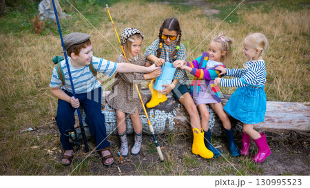 Group of children in rubber boots sharing watering can during outdoor play Group of children in rubber boots sharing watering can during outdoor play 130995523