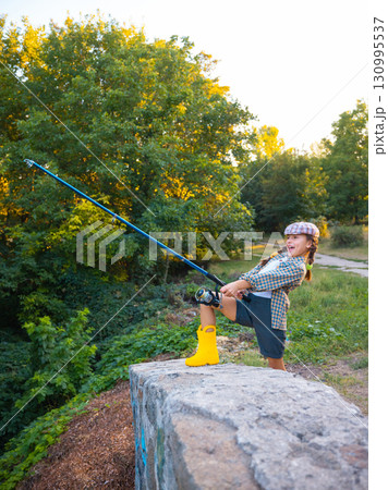 Happy girl in yellow boots fishing with rod on stone bridge Happy girl in yellow boots fishing with rod on stone bridge 130995537