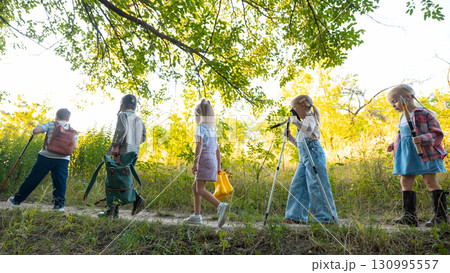 Group of kids hiking in green forest with backpacks and sticks Group of kids hiking in green forest with backpacks and sticks 130995557