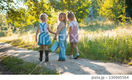Girls walking in forest holding hands with watering can in bright sunlight Girls walking in forest holding hands with watering can in bright sunlight 130995564