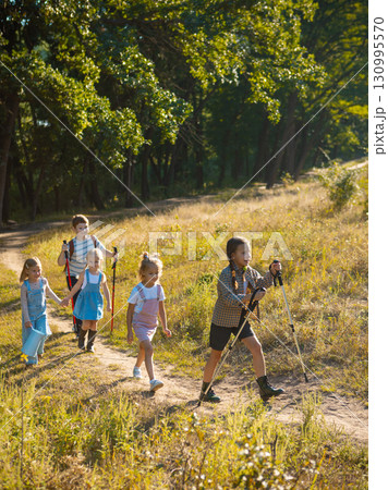 Kids walking with sticks and backpacks on sunny forest path 130995570