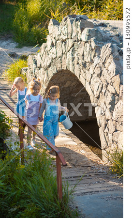 Group of little girls crossing small stone bridge holding hands and watering can Group of little girls crossing small stone bridge holding hands and watering can 130995572